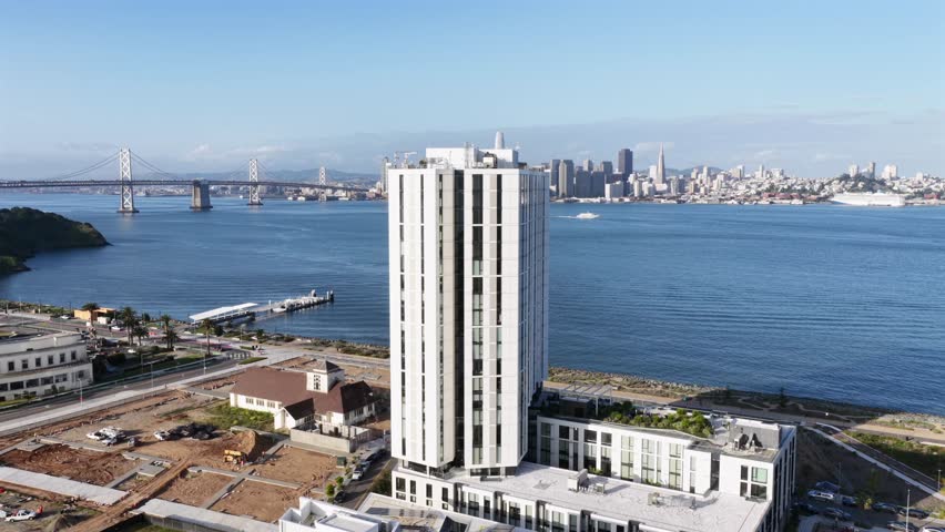 Luxury high-rise development on Treasure Island overlooking San Francisco Bay and skyline with Bay Bridge in background, modern waterfront architecture captured in United States. Aerial view wide.