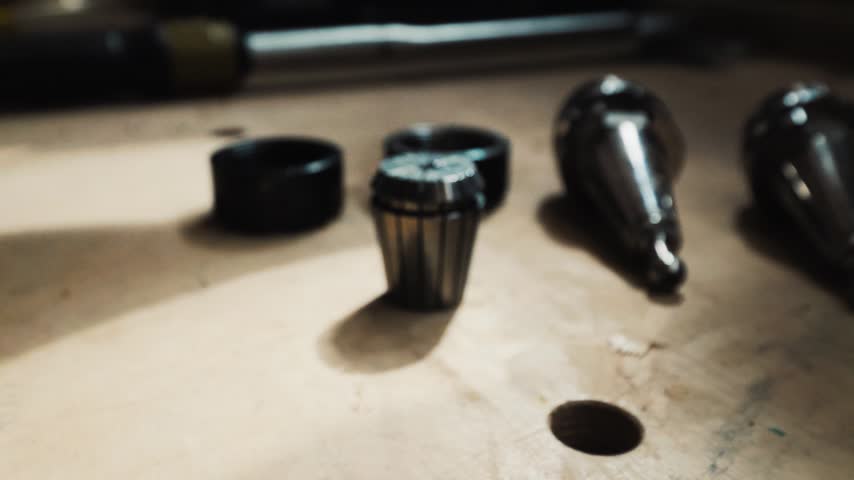 Set of router collets and tool holders laid out on a worktable in shallow focus.
