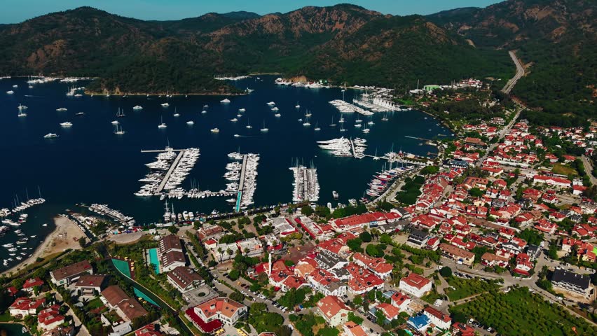 Aerial view of marina of Gocek Turkey with anchored yachts and boats in coastal bay town by hills and mountains.