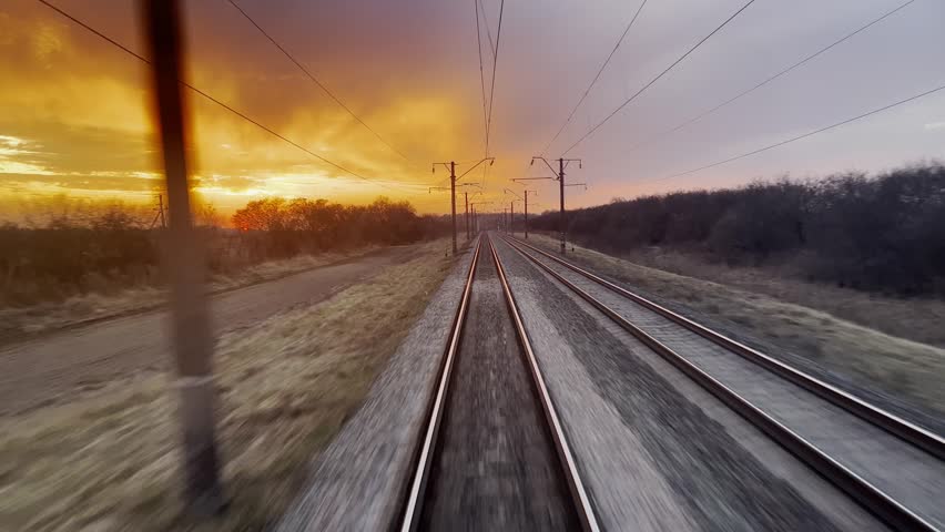 Moving train tracks, sunset sky, rural landscape, power lines.