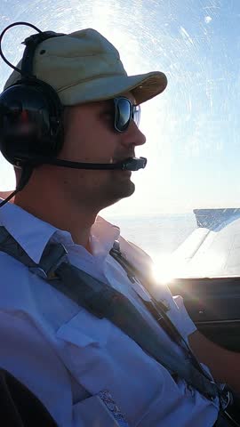 Pilot Flying Small Aircraft Cockpit with Avionics Dashboard and Clear Blue Sky Horizon. Young Male Pilot in Aviation Headset Controls Light Plane Cockpit During Daytime Flight