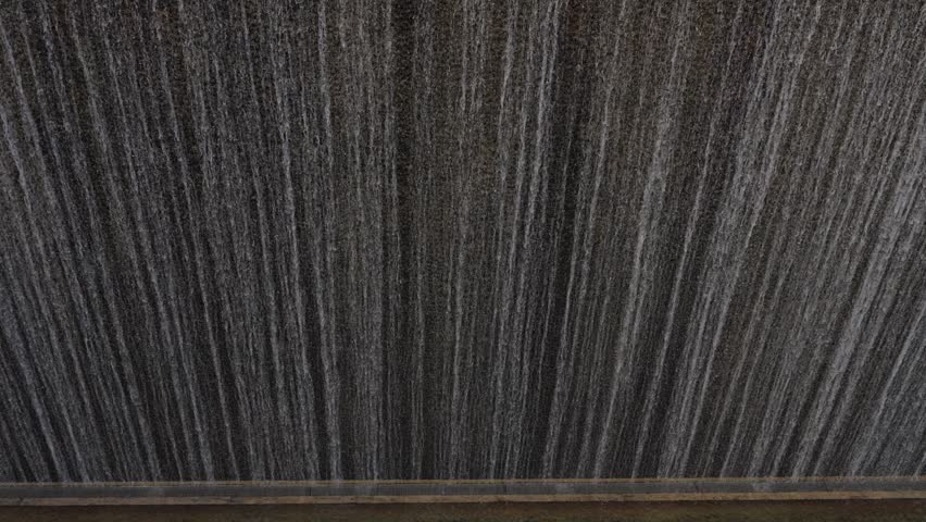 Dense water curtain falling in vertical streaks against dark surface with ledge at base