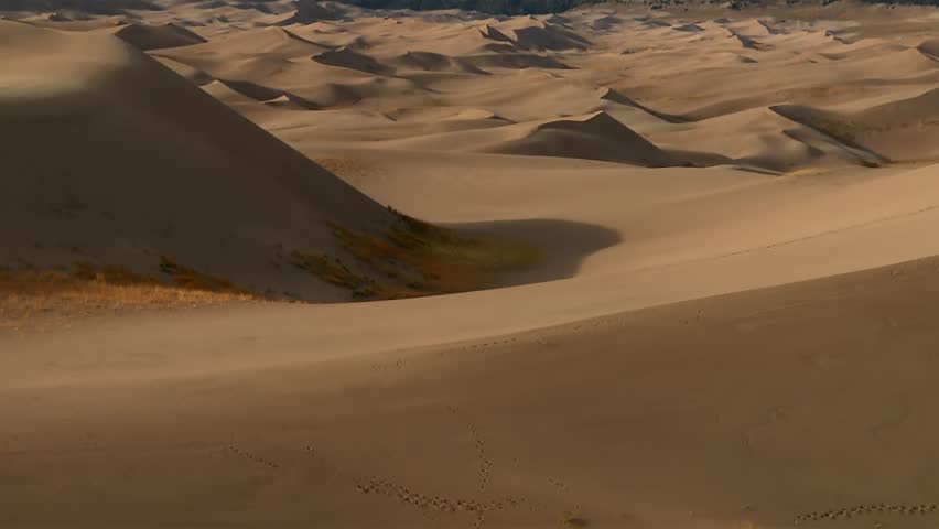 Sweeping sand dunes revealed against rugged snowcapped mountains in Great Sand Dunes National Park, tilt up shot.
