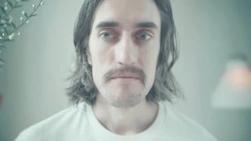 Lonely funny mustached guy smiling close-up of a young man with long dark hair and light eyes softly lit in a calm setting showing thoughtful expressions and ending with a gentle warm smile - Powered by Shutterstock - Get 15% off with code: PIKWIZARD15