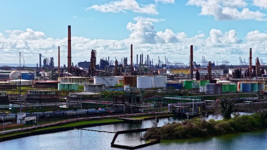 Aerial view of industrial area with factories, chimneys, and river on a partly cloudy day.