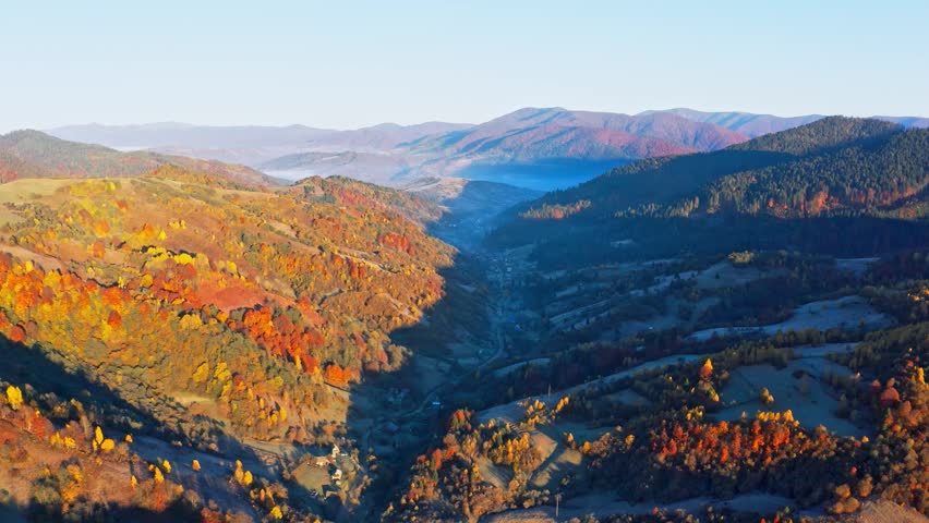 Shaded mountain valley with houses and forests at sunset