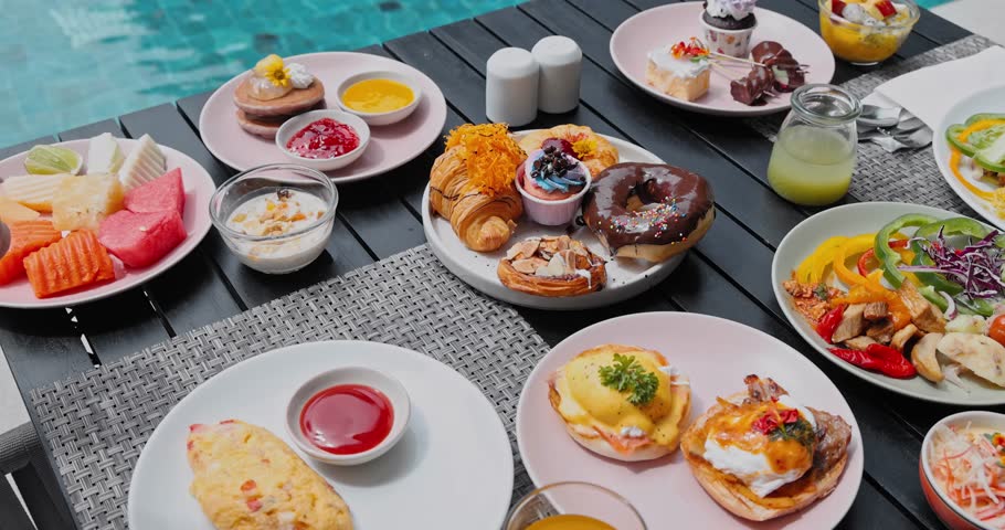 Hand reaching for almond pastry on wooden table full of varied food plates, outdoor resort pool background, overeating and luxury breakfast concept, binge eating lifestyle