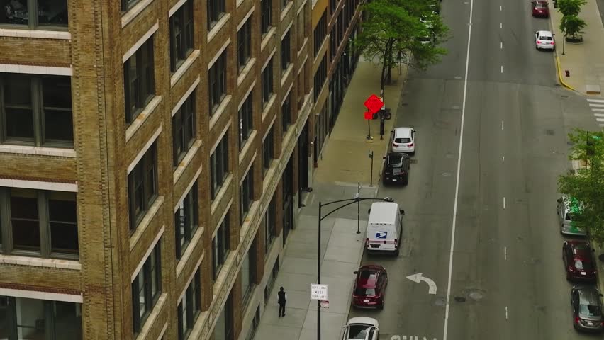 Vertical aerial perspective looking down at lush green trees lining a city street with parked cars and sidewalks in the West Loop area.
