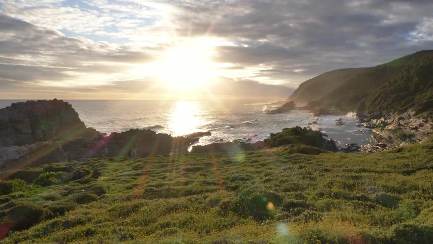 Breathtaking coastal landscape bathed in the warm glow of sunset, with dramatic cliffs, lush vegetation, and the ocean stretching to the horizon at Storm’s River Mouth in Tsitsikamma National Park.