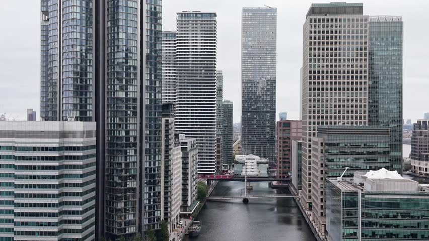 Aerial drone footage of a modern business district, featuring towering skyscrapers and a serene river, showcasing urban architecture and city life.