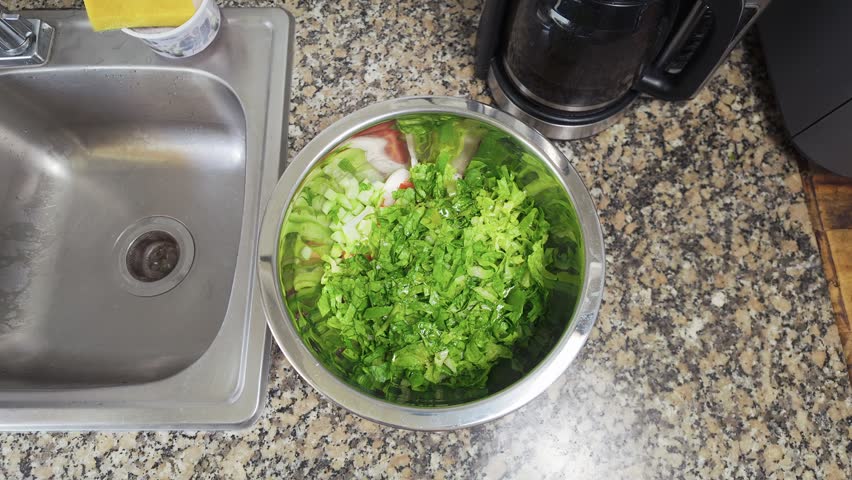 Top-down view of hands preparing a fresh organic salad. A person mixing lettuce, tomato, and other vegetables in a stainless steel bowl