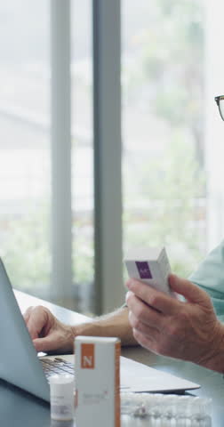Senior, medicine and man on video call by laptop in home for advice, information or dosage. Elderly patient, telehealth and technology with medication or tablets in house with glasses in retirement