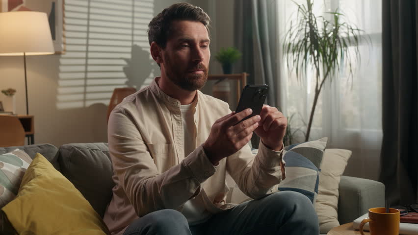 Unhappy upset Caucasian adult man looking in mobile phone negative shaking head reading bad news look sad at camera disappointed middle-aged male homeowner on sofa couch browsing smartphone at home