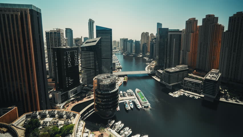 Cinematic timelapse of Dubai Marina skyline with boats gliding through water and shifting urban shadows among modern skyscrapers in daylight