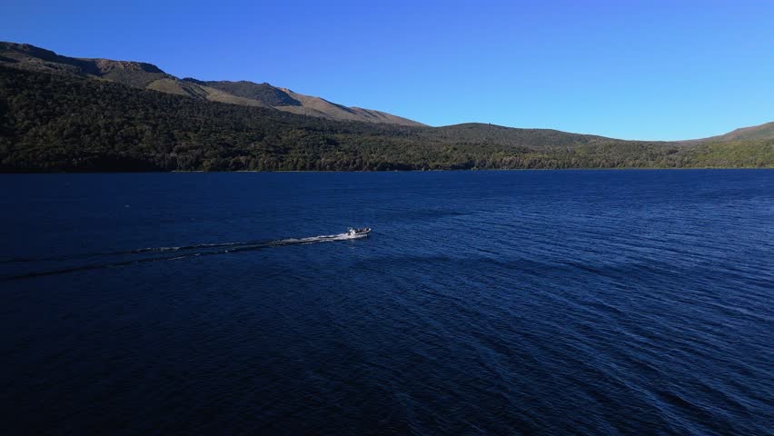 Small motorboat moves across a deep blue lake with green hills in background