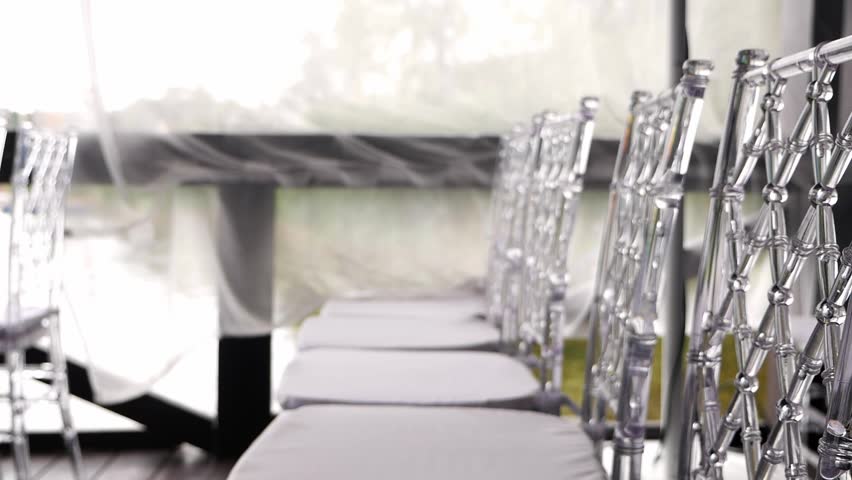 Close-up of rows of chairs with transparent backs at a wedding ceremony. Glass chairs.