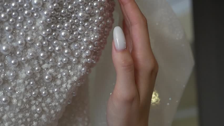Close-up of the bride tenderly touching her pearl wedding dress, which is hanging on a hanger. Beautiful morning of the bride.