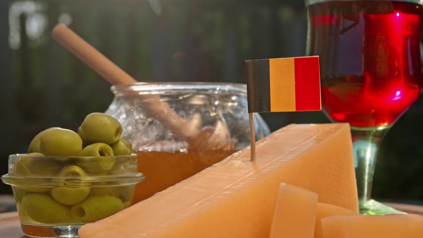 Belgian cheese, honey, and olives are arranged with rustic elegance beside rich red wine, creating warm European food travel atmosphere