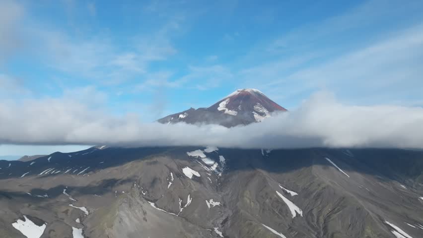 Aerial view of Avachinsky Volcano rising above a low cloud layer, with rocky ridges and snow patches under a clear blue sky in Kamchatka Krai, Russia