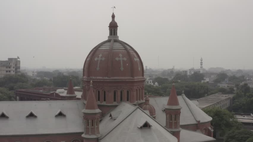 Historic Christian Church in Lahore Pakistan Cinematic Aerial View, Cinematic drone footage showcasing the historic Sacred Heart Cathedral in Lahore, Pakistan. The aerial view captures the magnificent red brick Gothic architecture, towering spires, cathedral dome, and surrounding urban cityscape in soft atmospheric light. Perfect for documentaries, travel films, architecture projects, religious content, heritage visuals, tourism promotions, cinematic establishing shots, and editorial storytelling.