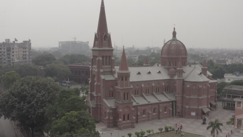 Beautiful Aerial View of Historic Cathedral Church in Lahore, Cinematic drone footage showcasing the historic Sacred Heart Cathedral in Lahore, Pakistan. The aerial view captures the magnificent red brick Gothic architecture, towering spires, cathedral dome, and surrounding urban cityscape in soft atmospheric light. Perfect for documentaries, travel films, architecture projects, religious content, heritage visuals, tourism promotions, cinematic establishing shots, and editorial storytelling.