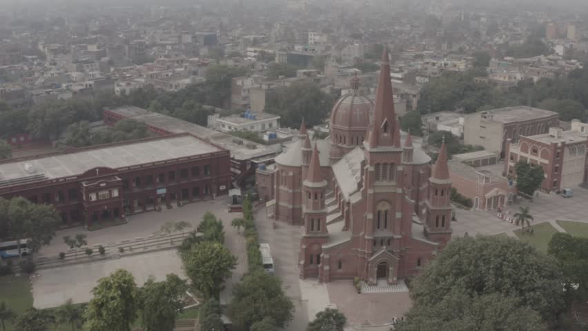 Historic Christian Landmark in Lahore Pakistan Drone Footage, Beautiful cinematic drone footage of Sacred Heart Cathedral in Lahore, Pakistan, featuring stunning Gothic architecture, tall church spires, red brick exterior, and the surrounding urban cityscape. Captured from an aerial perspective in soft atmospheric light, this historic Christian landmark showcases the architectural heritage and religious significance of Lahore. Ideal for documentaries, travel films, religious content, tourism projects, editorial visuals, and cinematic establishing shots.