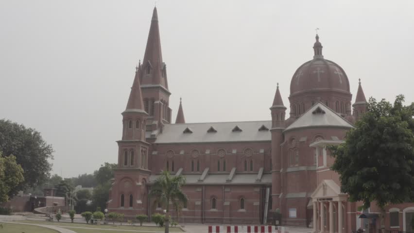 Historic Christian Landmark in Lahore Pakistan Drone Footage, Beautiful cinematic drone footage of Sacred Heart Cathedral in Lahore, Pakistan, featuring stunning Gothic architecture, tall church spires, red brick exterior, and the surrounding urban cityscape. Captured from an aerial perspective in soft atmospheric light, this historic Christian landmark showcases the architectural heritage and religious significance of Lahore. Ideal for documentaries, travel films, religious content, tourism projects, editorial visuals, and cinematic establishing shots.