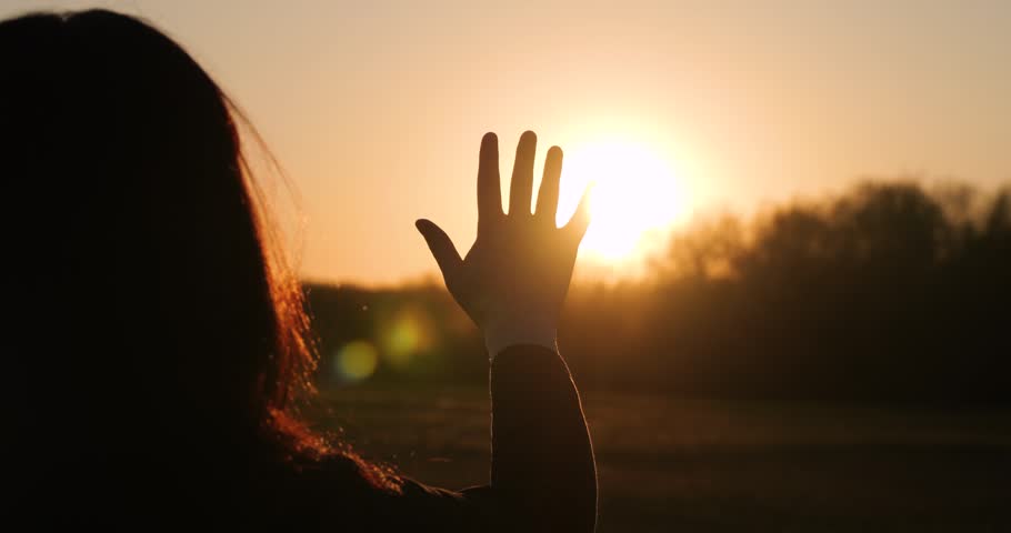 Silhouette of woman enjoying sunset. Girl raises hand to sun, embracing nature