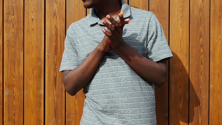 Man stands against wooden wall and claps hands while smiling during a sunny day in the park