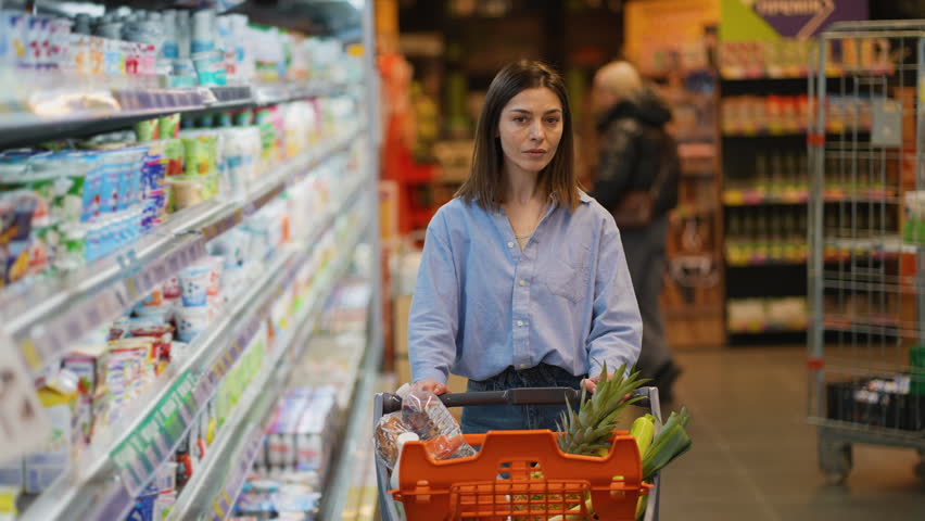 Happy young woman pushing shopping cart in supermarket aisle