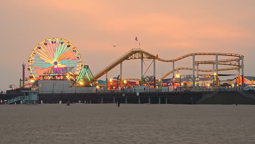 Santa Monica Pier At Sunset With Ferris Wheel Lights, cinematic coastal video frame with amusement rides and warm sky