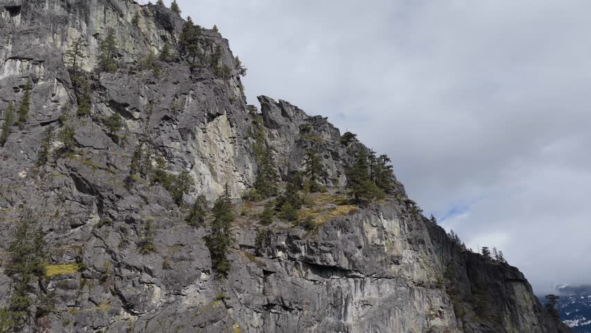 Majestic Mountain Peaks with Rugged Rock Faces and Pine Trees Under a Cloudy Sky in British Columbia, Canada