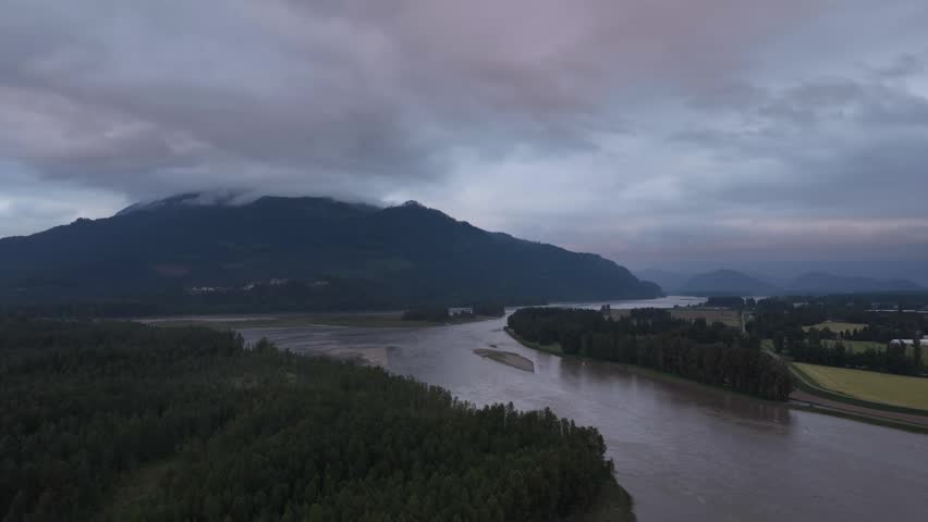 Dramatic Aerial View Of River And Forest Against Cloud-Covered Mountains In British Columbia, Canada
