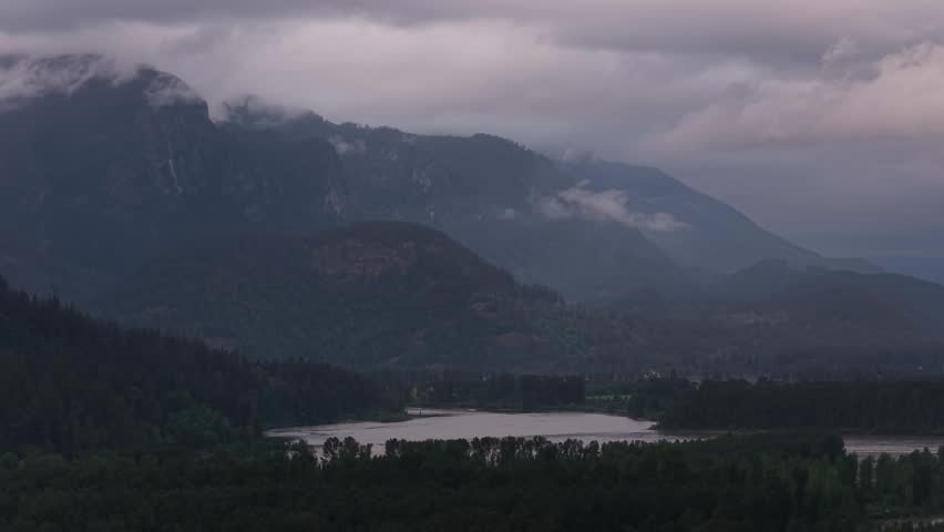 Dramatic Cloudy Mountains Over a Serene River and Lush Forest in British Columbia, Canada