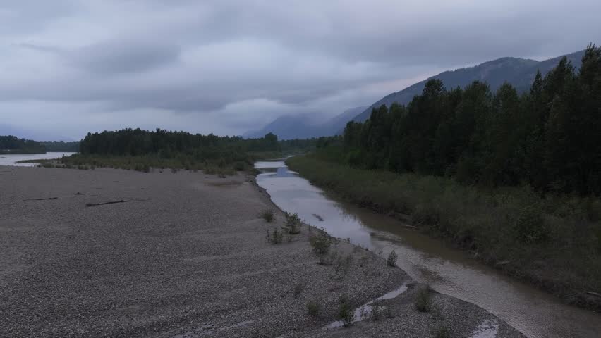 Tranquil River Winding Through Forest and Mountains in British Columbia, Canada on a Cloudy Day