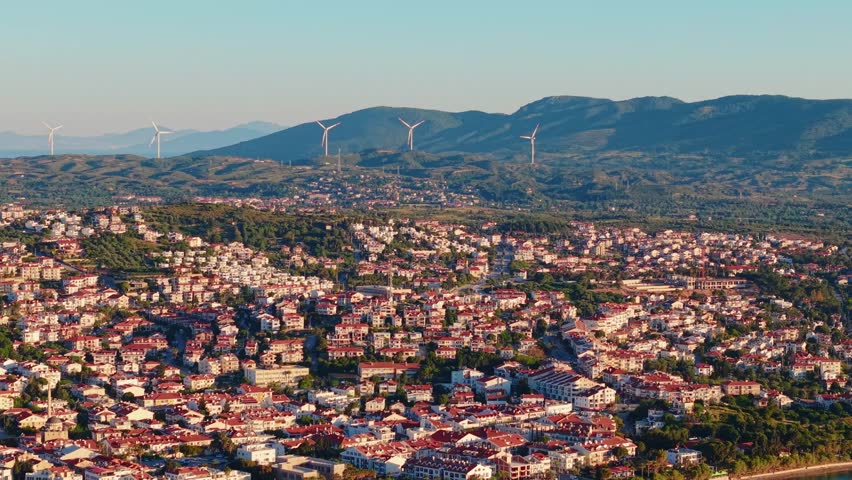 Aerial view of residential town spreading across foothills toward wind turbines , marina of Datcha Turkey.