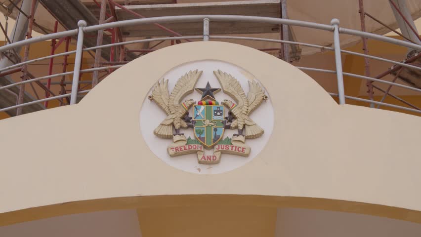 Close up of coat of arms of Ghana with motto Freedom and Justice, national emblem with golden eagles and black star on government building wall in Accra, Africa