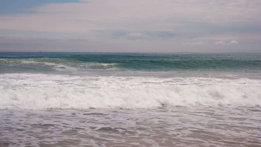 Large ocean waves crashing on a sandy beach under a cloudy sky.
