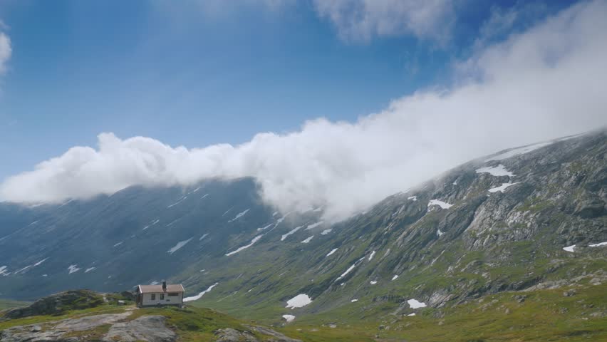 Isolated cabin, mountain view, cloudy sky, rocky terrain, nature scene.
