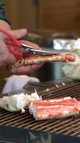 Close-up shot of a vendor cutting red king crab legs with scissors over a grill