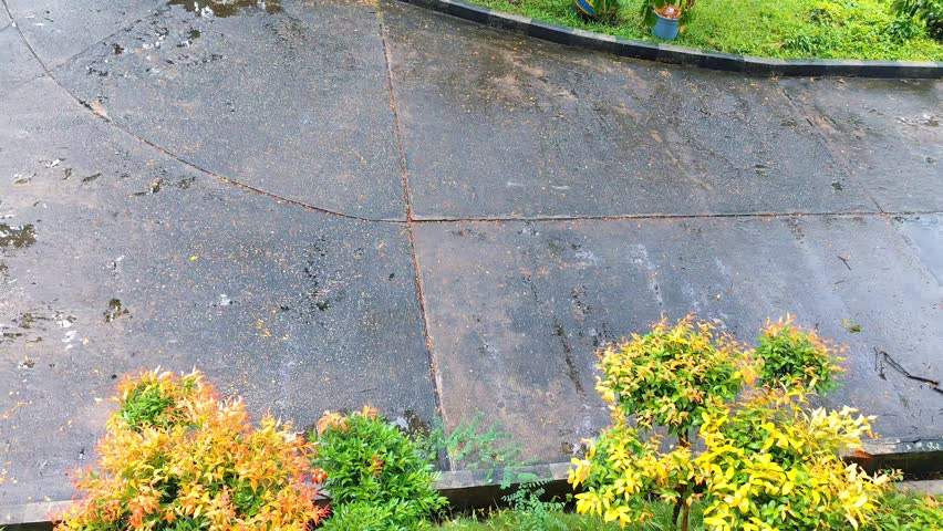 High-angle view of a wet concrete driveway and parking area in a garden after rain, with puddles reflecting the sky