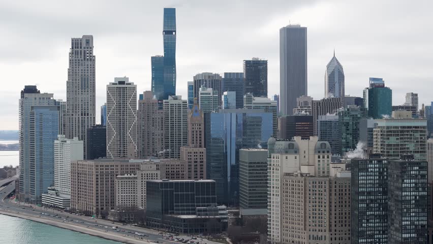 Aerial view of chicago skyline along lake michigan, showcasing impressive skyscrapers and active traffic flow on a cloudy day, capturing architectural grandeur and urban motion.