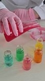 A person wearing gloves pours a red liquid from a flask into a bowl. Several glass containers with different colored liquids are visible on the table. The activity showcases mixing experiments. - Powered by Shutterstock - Get 15% off with code: PIKWIZARD15
