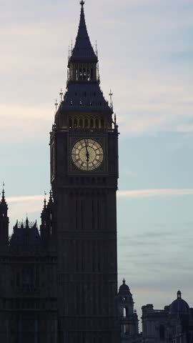 Famous London landmark Big Ben clock tower, officially known as Elizabeth Tower, showing the time with its historic illuminated dial against a beautiful evening sky with soft clouds passing