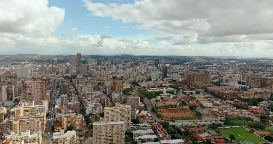 4K aerial zoom in shot over Johannesburg city center. High-angle drone footage showing dense urban architecture, skyscrapers, and street layouts of South African metropolitan neighborhood.