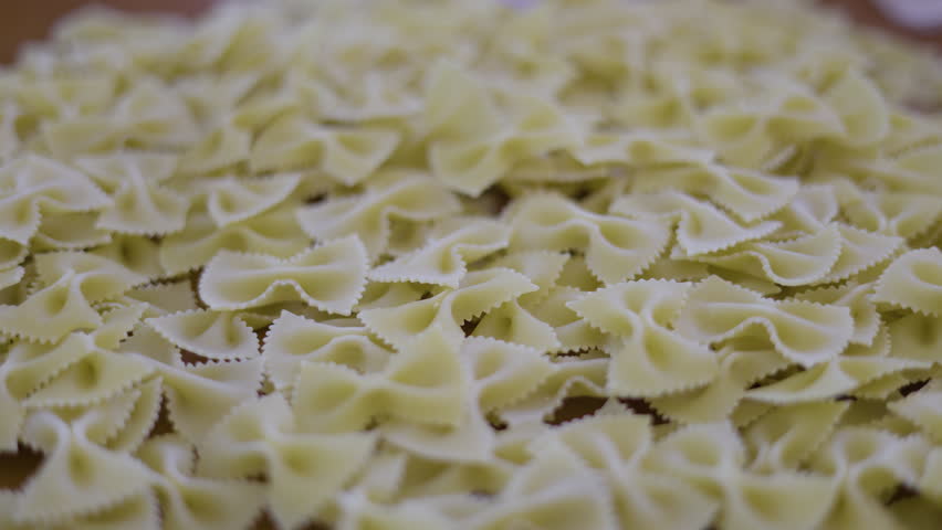 Uncooked Bow Tie Pasta On Table Dry. Close up of farfalle macaroni dropping into a ceramic bowl, suitable for italian food commercials or cooking tutorial videos.