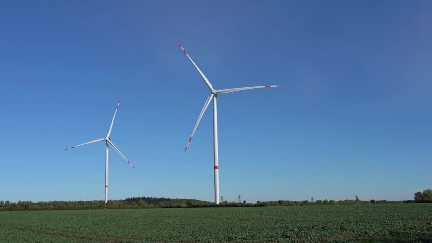 Two modern wind turbines standing in a green field under a clear blue sky