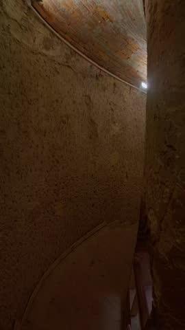 Vertical handheld footage of narrow underground corridor with rough stone walls and a curved passage leading into darkness. Catacombs of Kom El Shoqafa in Alexandria, Egypt