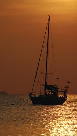 Sailboat silhouetted against orange sky water reflection.