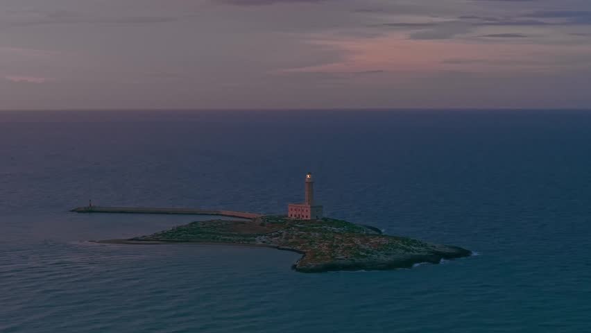 Aerial view of the Vieste historic lighthouse at night in Puglia, Italy, illuminated coastal landmark on the Mediterranean Sea with dramatic shoreline, maritime heritage, and dark seascape.